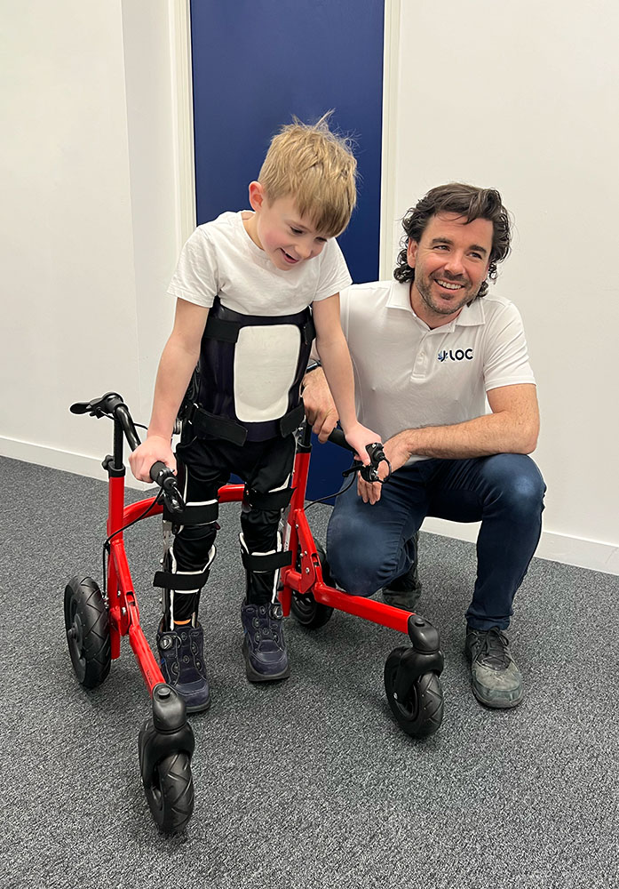 Sam Walmsley with Ted wearing his Reciprocating Gait Orthosis and walker at the London Orthotic Consultancy