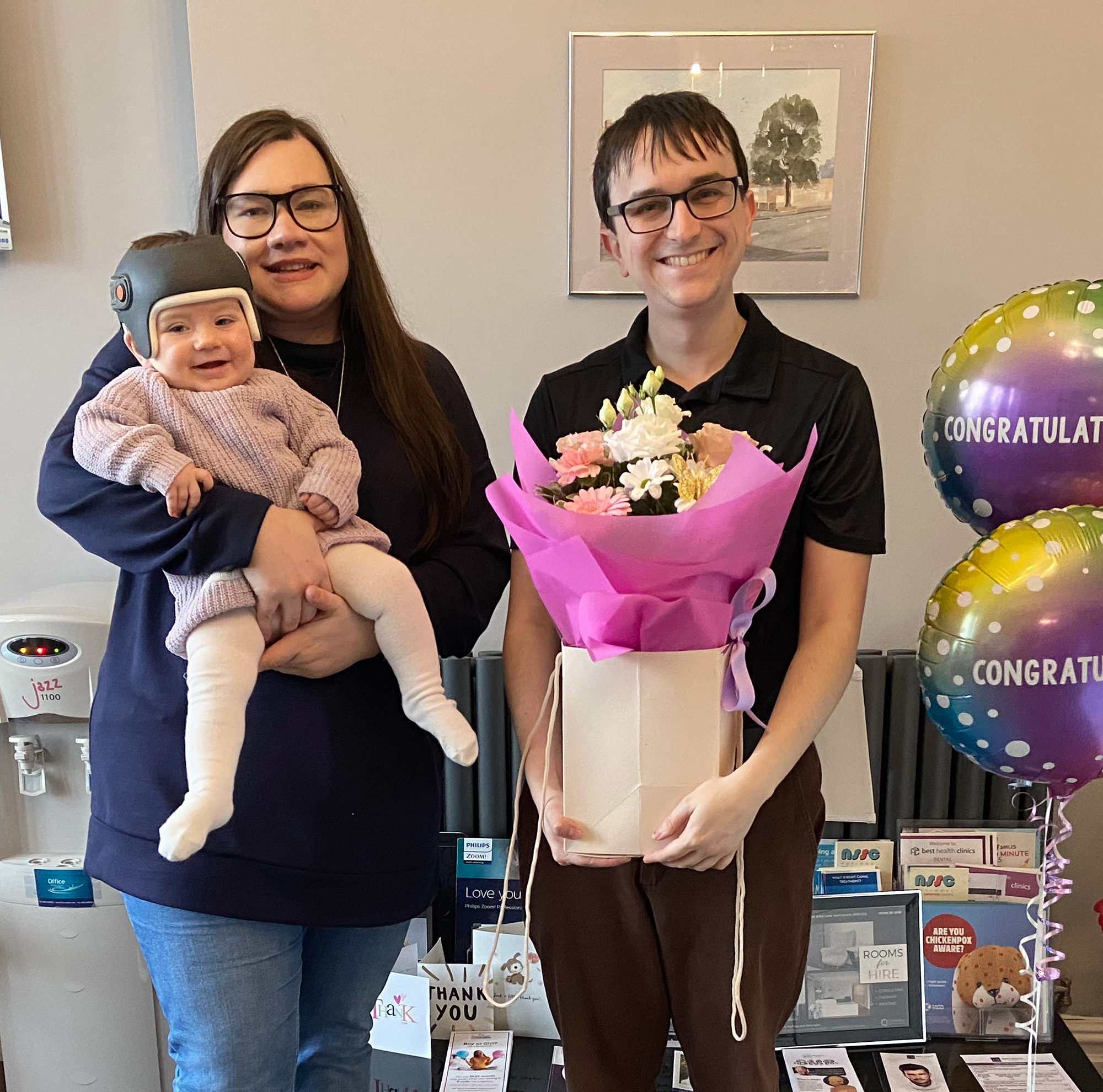 Mum Stephanie with baby Autumn in her plagiocephaly helmet standing next to George Coles celebrating her helmet graduation